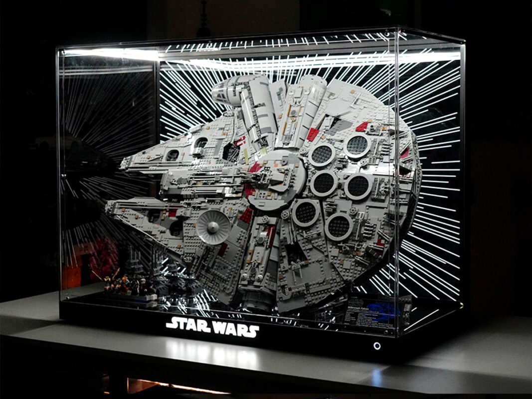 LEGO Millennium Falcon model inside a glass display case, illuminated backdrop with starburst lines and a Star Wars logo at the base.