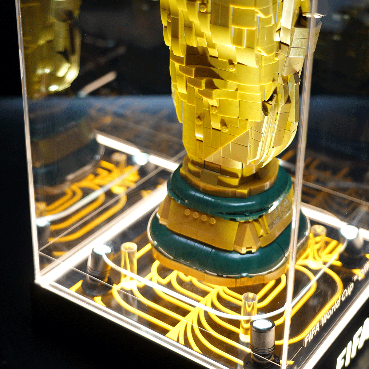 LEGO-built FIFA World Cup trophy replica inside a glass display case with a yellow base and intricate brickwork.
