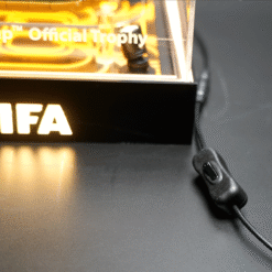 Glowing trophy with 'Official Trophy' text inside, base shows 'IFA' in bright letters, connected to a USB power adapter.