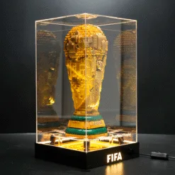 Gold LEGO replica of the FIFA World Cup trophy displayed in a clear glass case on a black pedestal with 'FIFA' lit on the base.