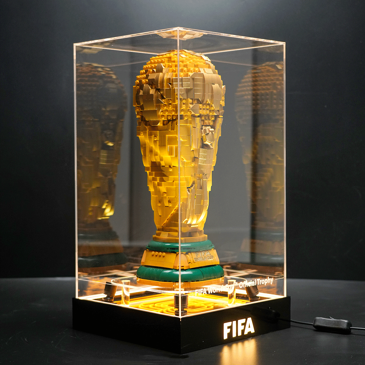 Gold LEGO replica of the FIFA World Cup trophy displayed in a clear glass case on a black pedestal with 
