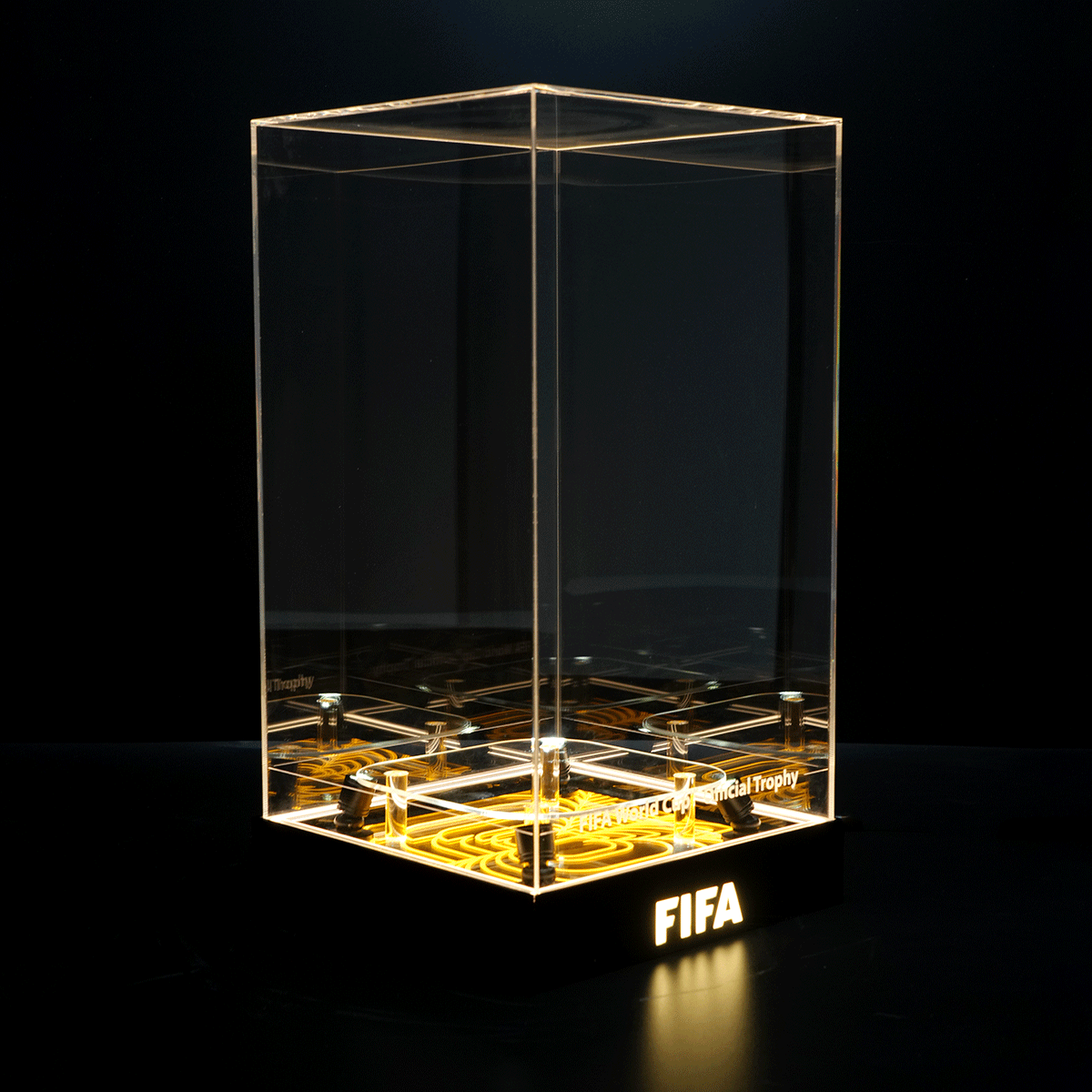 Clear glass display case on a lit black base with the FIFA logo, empty inside.