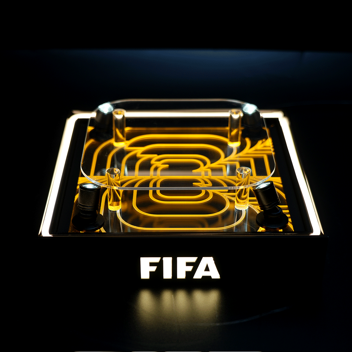 FIFA-branded display: a glass case with yellow neon looping patterns inside, set on a lit black pedestal with the word FIFA glowing below.