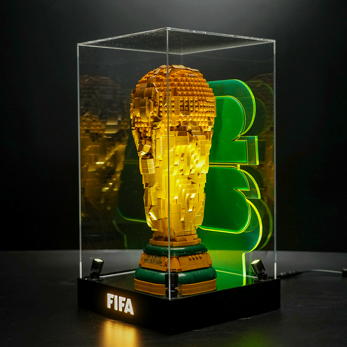 LEGO-style FIFA World Cup trophy in a glass display case with a black base labeled FIFA and green neon number 3 behind it.