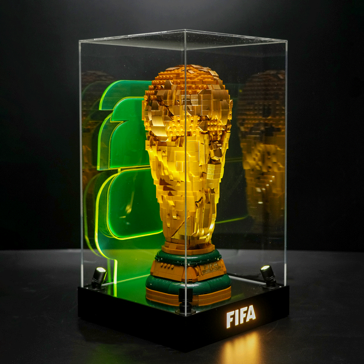 Gold LEGO-style FIFA World Cup trophy model displayed in a glass case with neon green background accents.