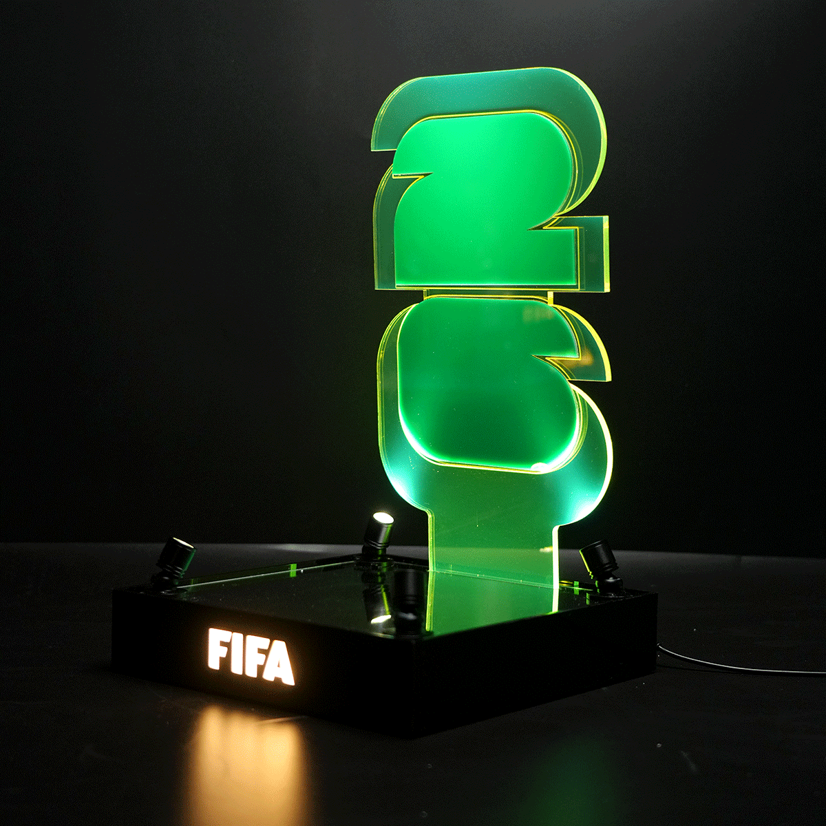 Green neon FIFA trophy on a black base, glowing against a dark background