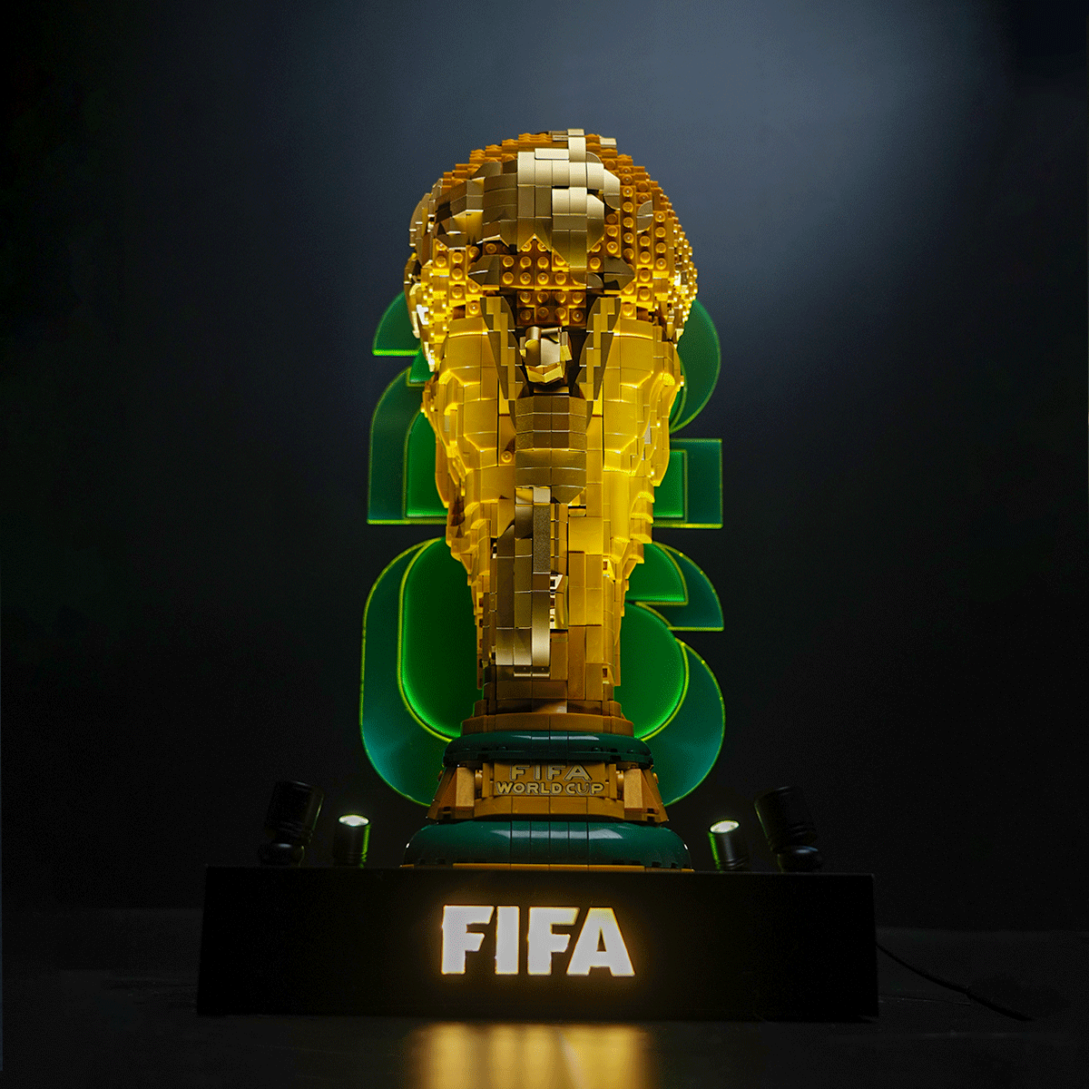 Gold LEGO sculpture of the FIFA World Cup trophy on a dark stage with a glowing 'FIFA' pedestal behind it.