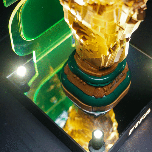 Close-up of a multi-colored LEGO sculpture (yellow, tan) on a green circular pedestal, inside a glass display case.