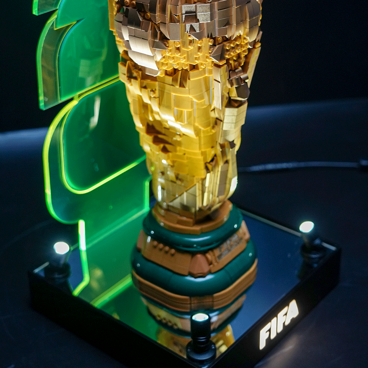 Pixelated gold trophy sculpture on a mirrored base with green neon lighting and 'FIRA' label.