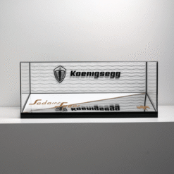 Glass display case with black frame on a white shelf showing a Koenigsegg logo and brand name on the back panel.