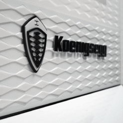 Koenigsegg logo badge on a white textured wall with a shield emblem and bold wordmark.