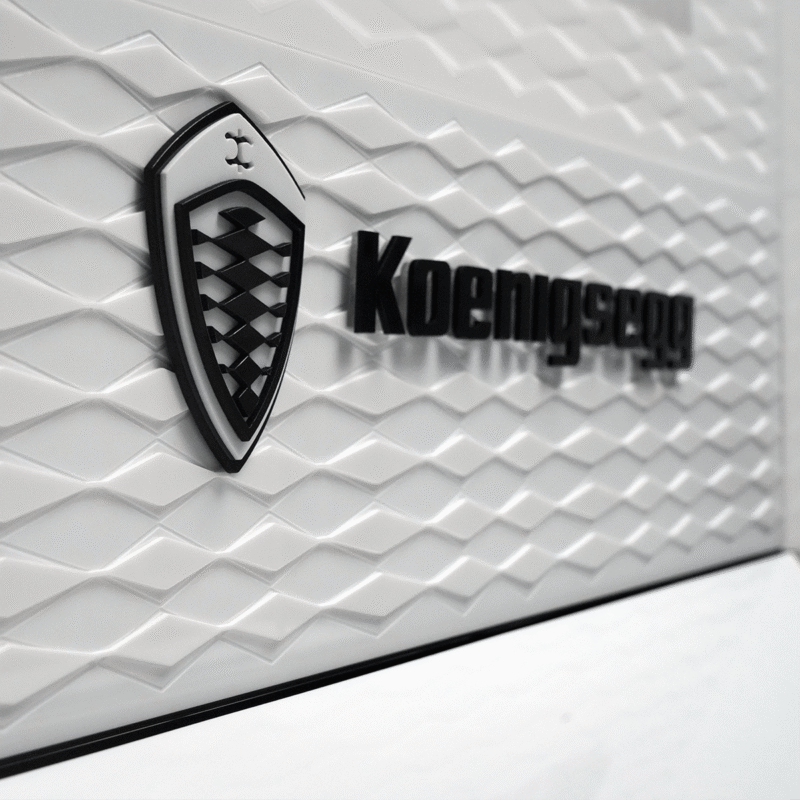 Koenigsegg logo badge on a white textured wall with a shield emblem and bold wordmark.