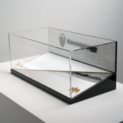 Clear glass display case with a black base sitting on a white surface, empty inside.