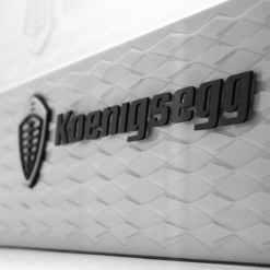 Close-up of a Koenigsegg badge on a white textured car surface with a diamond pattern