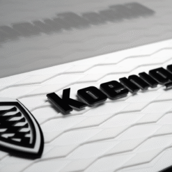 Close-up of the Koenigsegg badge on a white textured car hood.