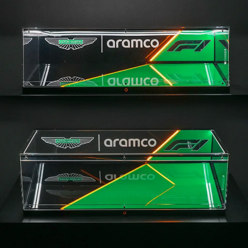 Two clear glass display cases mounted on a dark wall feature Aston Martin and Aramco branding with green and orange neon diagonal accents.