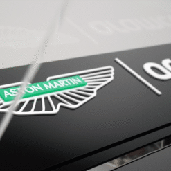Close-up of an Aston Martin emblem with a green badge and white wings on a glossy black surface, likely a car hood.