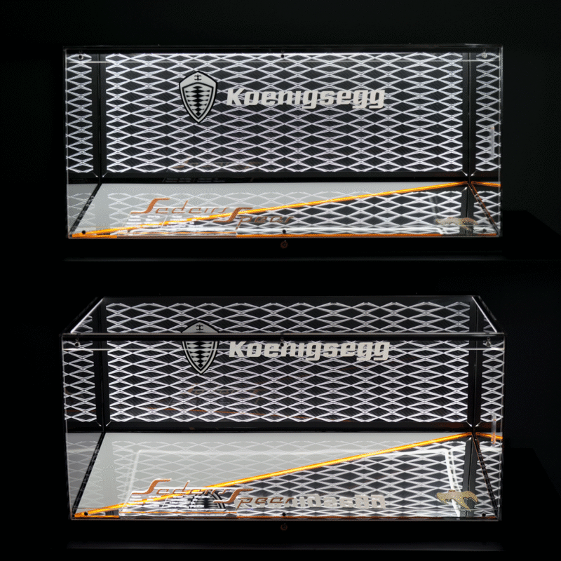 Two reflective display panels with a diamond-patterned grille, Koenigsegg logo and shield, and an orange diagonal accent against a dark background.