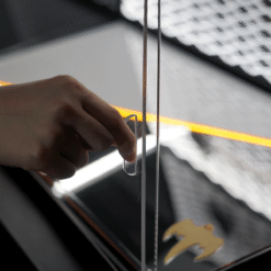 Close-up of a hand sliding a thin clear plastic card between glass panels, with an orange light strip in the background.