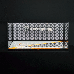 Koenigsegg branding on a silver lattice display with orange bottom light and a reflective surface.