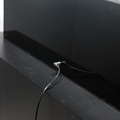 Close-up of a small coaxial-like connector plugged into the back of a black flat-screen display on a dark shelf.