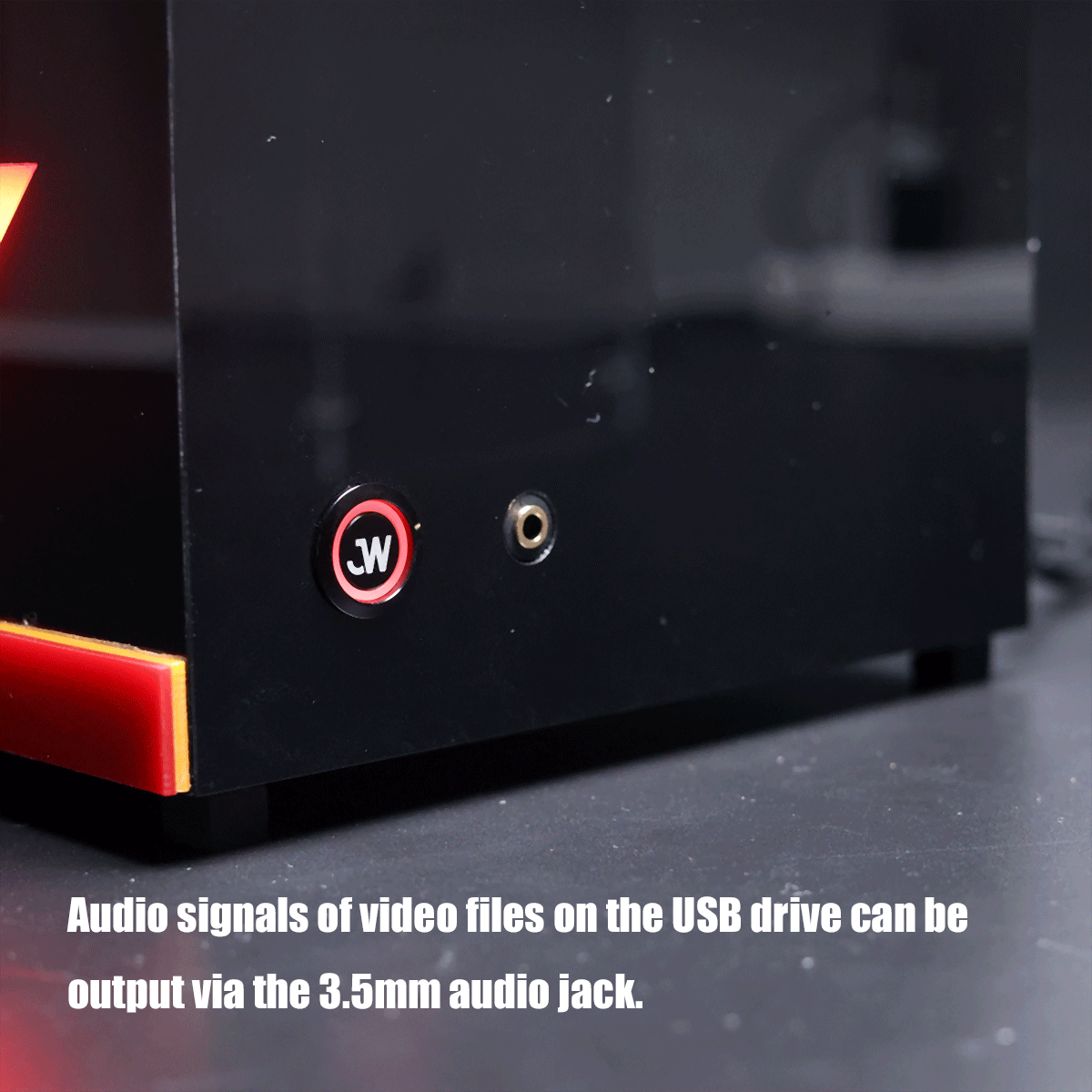 Close-up of a black electronic device showing a red JW power button and a 3.5 mm audio jack beside it, indicating audio output from a USB drive.