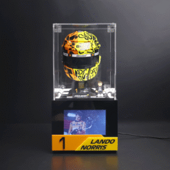 Yellow and black McLaren race helmet in a clear glass display case on a black pedestal, with a small Lando Norris figure beside a '1' podium sign.