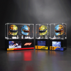 Display of four McLaren F1 helmet replicas in glass cases on a black pedestal, with mini figures and race banners beneath the cases.