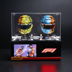Two McLaren F1 helmets in a glass display case, yellow/black and blue/orange patterns, with small figurines in front and a screen showing team imagery.