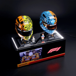 Two brightly colored Formula 1 helmets on a glossy display stand with mini-figures and McLaren branding, set against a dark background.