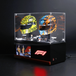 Two colorful racing helmets in a clear display case on a black pedestal with F1 branding nearby.