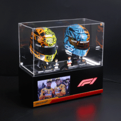 Clear display case containing two colorful McLaren Formula 1 helmets (orange and blue), small figurines, and a photo panel on a black pedestal.