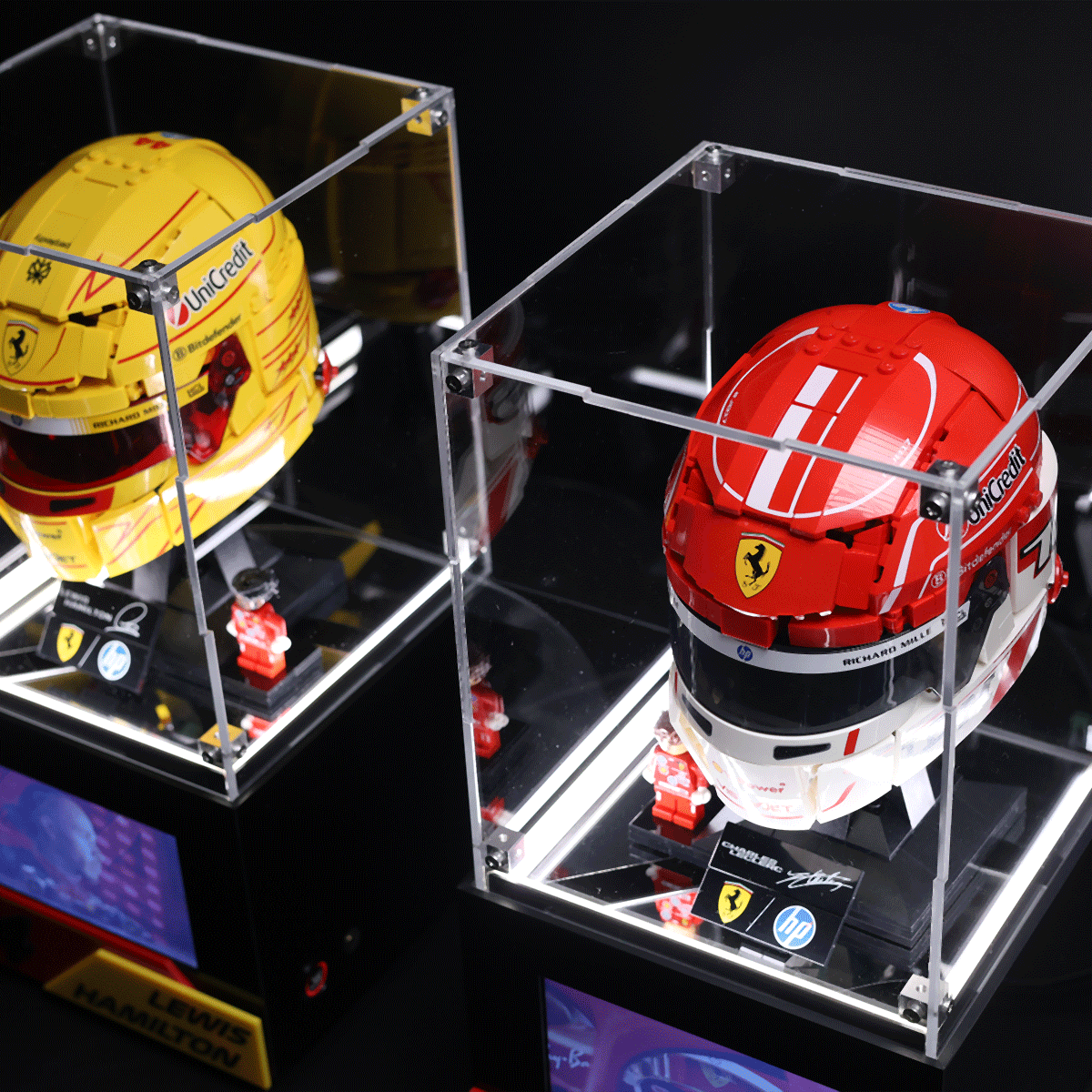 Pair of Formula 1 helmets in clear display cases, yellow and red Ferrari styles with team logos, on an exhibit shelf