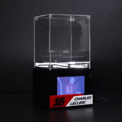 Clear acrylic display case on a black base with a small screen showing a racing driver, labeled '16 Charles Leclerc' in red and white.