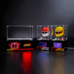 Three clear display cases holding red and yellow Formula 1 helmets with nameplates—Leclerc 16 and Hamilton 44—against a dark backdrop.
