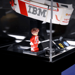 LEGO minifigure in a red racing suit standing on a display base beside a white and red race car model with sponsor branding.