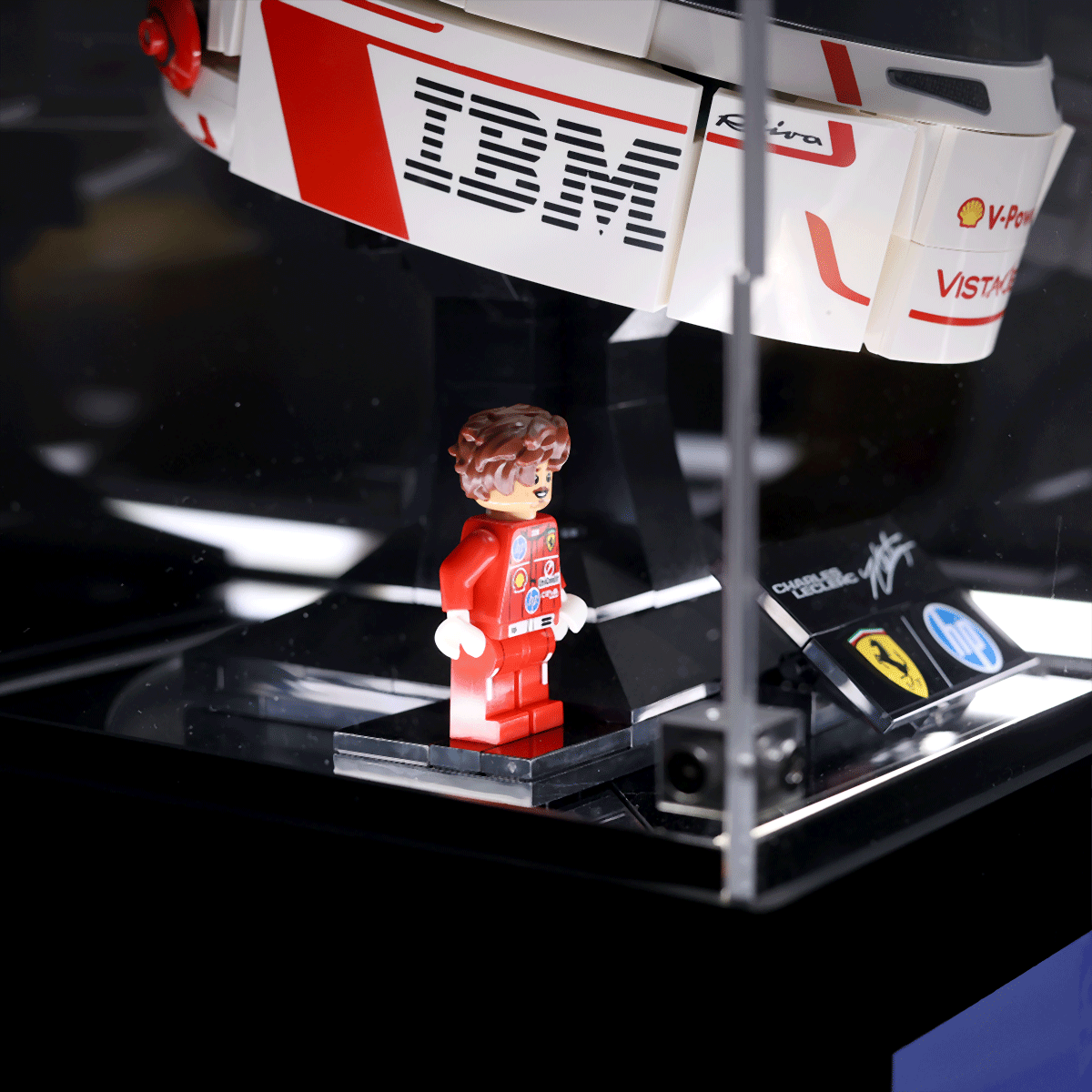 LEGO minifigure in a red racing suit standing on a display base beside a white and red race car model with sponsor branding.