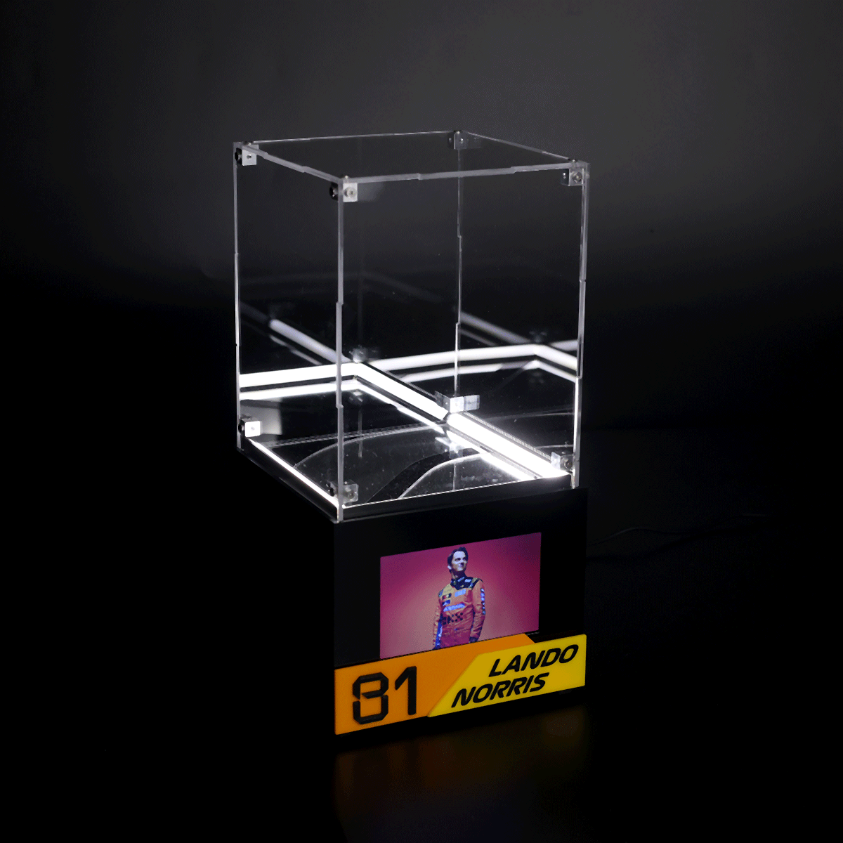 Transparent acrylic display case on a black pedestal, illuminated from within, with a small photo and a yellow 81 Lando Norris plaque at the base.