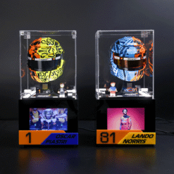 Two Formula 1 helmets displayed in glass cases on stands, with small driver figurines and nameplates for Oscar Piastri (left) and Lando Norris (right).