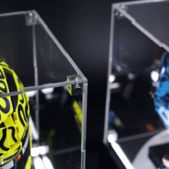 Close-up of a clear acrylic display case joined with metal brackets, housing a neon-yellow numbered helmet inside.