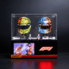 Two brightly patterned McLaren F1 helmets in a glass display case, flanked by small figurines, on a black pedestal with an F1 display beneath.
