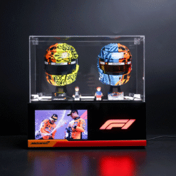 Two brightly patterned McLaren F1 helmets in a glass display case, flanked by small figurines, on a black pedestal with an F1 display beneath.