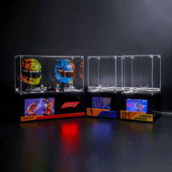 Two clear display cases on a black podium, left case holding colorful racing helmets and figures, right case empty, with race-themed screens and podium plaques nearby