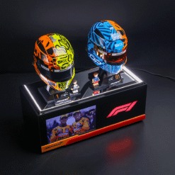 Two colorful Formula 1 helmets displayed on a black podium with miniature figures and a small photo panel, McLaren branding visible in the scene.